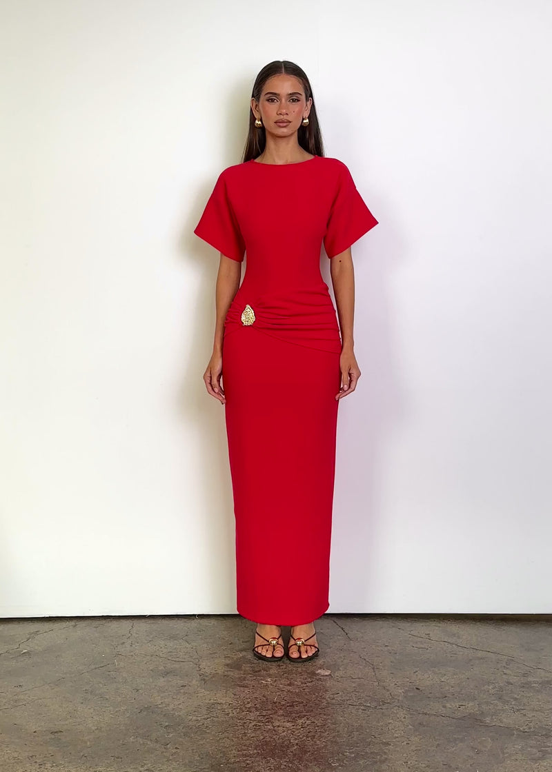 Video: Tallie Maxi Dress in Red with a round neckline, fitted bodice, relaxed short sleeves, ruched waist detailing with a statement gold embellishment and a streamlined ankle-length silhouette.
