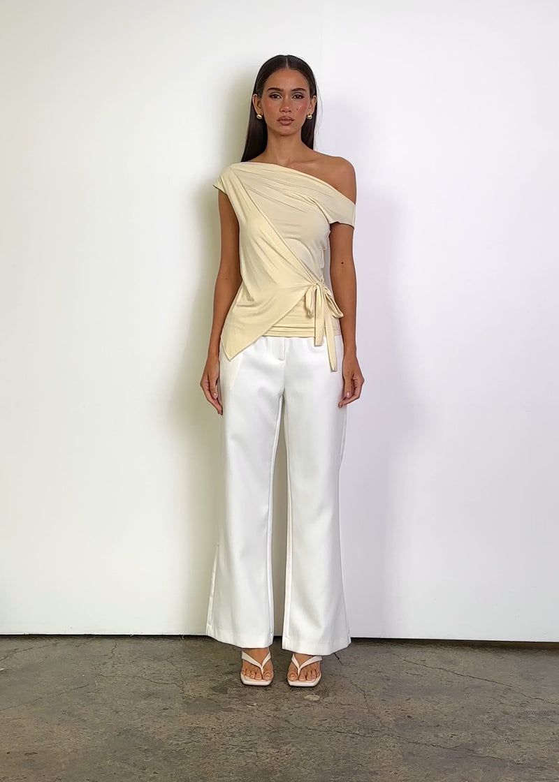 Video: Tanya Asymmetric Top in Cream, featuring an asymmetric off-shoulder neckline, fitted silhouette, soft draped overlay and a side tie detail at the waist.