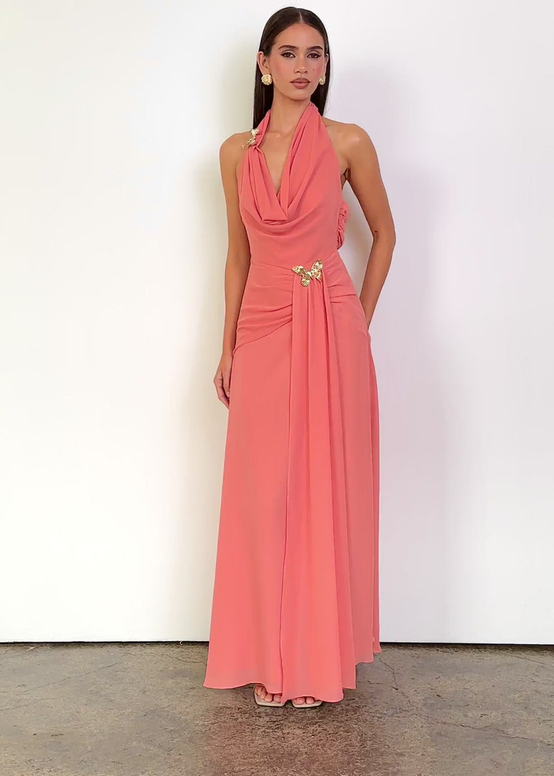 Video: Kimana Halter Maxi Dress in Coral, featuring a draped cowl halter neckline, sleeveless design, fitted gathered waist, statement gold butterfly details and a flowing maxi-length silhouette.