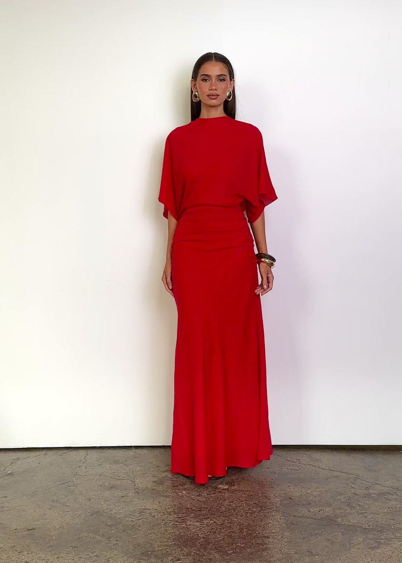 Video: Yasminne Maxi Dress in Cherry Red with a high round neckline, relaxed draped bodice, flowing cape-style short sleeves, fitted ruched waist and a floor-length skirt with a soft fluid finish.