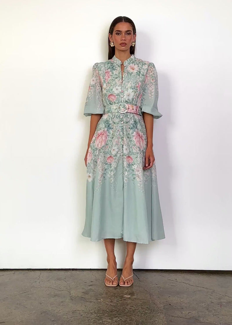 Video: Saydie Midi Dress with Belt in Seafoam Peony, featuring a high collar neckline, front button detailing, puff sleeves, a fitted waist with matching statement buckle belt, and a flowing A-line midi silhouette in a soft pink and green floral print.