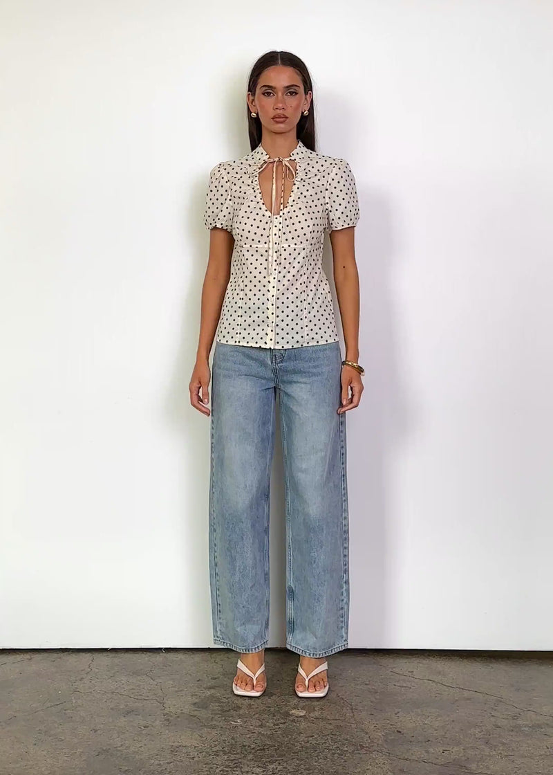 Video: Madelin Top in Cream Polka Dot with a fitted silhouette, collared neckline with keyhole opening and tie detail, softly gathered puff short sleeves, front button detailing and a hip-length hem.