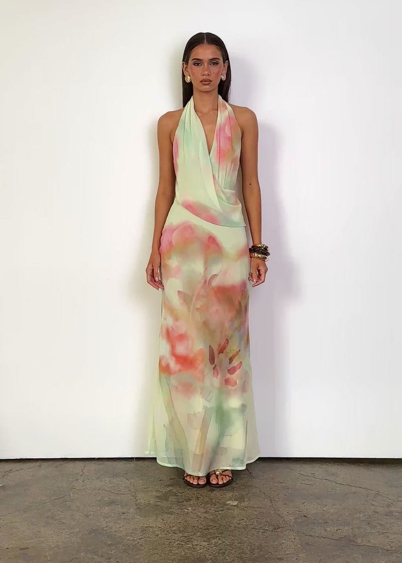 Video: Harpah Halter Maxi Dress in Pastel Paradise with a plunging halter neckline, sleeveless design and softly draped wrap-style bodice, featuring a fitted waist and flowing maxi-length silhouette in a sheer pastel floral print.